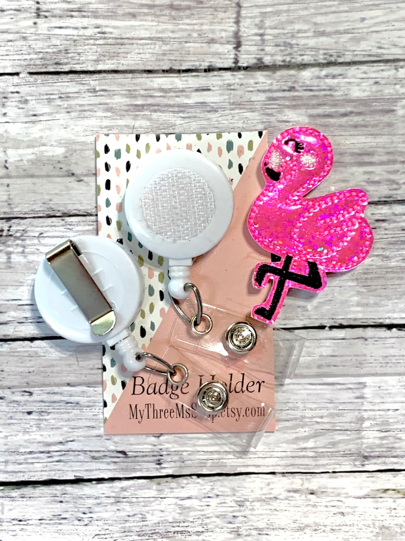 May include: Pink glitter flamingo badge holder with a white retractable badge reel and a clear plastic badge holder. The badge holder has the text "Badge Holder" and "MyThreeMsCraftsy.com".