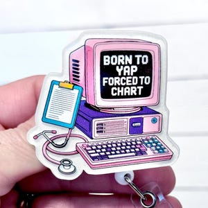May include: A pink and purple computer-themed badge reel with the text "BORN TO YAP FORCED TO CHART." The design includes a computer monitor, keyboard, stethoscope, and clipboard. The badge reel is attached to a white retractable clip.