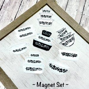 May include: A collection of white and black Pyrex dish magnets with a floral design. The magnets are in various shapes and sizes, including rectangular and round. The text "~ Magnet Set ~" is at the bottom of the image.