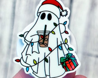 May include: A white ghost-shaped badge reel with a Santa hat, holding a drink and a wrapped gift. The ghost is decorated with colorful Christmas lights. The badge reel is attached to a white retractable cord.