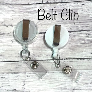 May include: Two white retractable badge holders with clear plastic straps and belt clips. The badge holders have a silver metal clip and a clear plastic window.