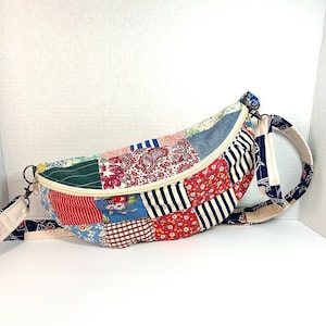 May include: A crescent-shaped crossbody bag constructed from a patchwork of various fabrics, including red, blue, and white floral, striped, paisley, and gingham patterns. The bag features a cream-colored zipper closure and an adjustable fabric strap.