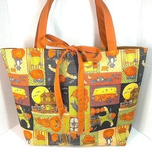 May include: A fabric tote bag featuring a patchwork Halloween print with pumpkins, scarecrows, bats, and haunted houses in orange, black, yellow, and green. The bag has two orange shoulder straps and an orange fabric tie closure at the top centre.