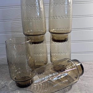 Può includere: Set di sei bicchieri ambrati. Ogni bicchiere ha una forma cilindrica con un motivo testurizzato a forma di onda. I bicchieri hanno una base marrone scuro e sono impilati. Adatto per acqua, succo o altre bevande.