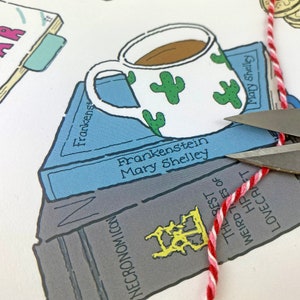 May include: A white coffee mug with green cactus designs sits on top of a stack of books. The books are titled "Frankenstein" by Mary Shelley and "The Rest of Weird Tales of HP Lovecraft". A red and white string is being cut with scissors.