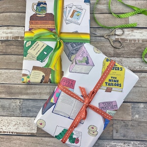 May include: Two gift wrapped packages with white wrapping paper featuring illustrations of books and book titles. The wrapping paper on the left package has a yellow, green, and white ribbon. The wrapping paper on the right package has an orange ribbon. The book titles on the left package include "The Return of the King", "The Two Towers", "The Fellowship of the Ring", "The Wind in the Willows", and "Harry Potter". The book titles on the right package include "The Nine Tailors", "Terry Pratchett", "Douglas Adams", and "The Very Hungry Caterpillar".