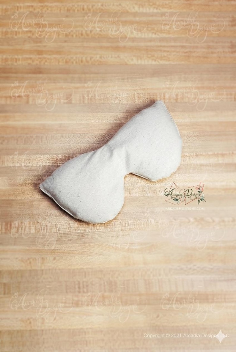 Pu&ograve; includere: Un cuscino bianco per gli occhi, sagomato per adattarsi al viso, &egrave; appoggiato su una superficie di legno marrone chiaro. Il cuscino &egrave; realizzato in un tessuto morbido e di colore chiaro. Il design &egrave; semplice e funzionale, suggerendo un focus sul relax e sul comfort.