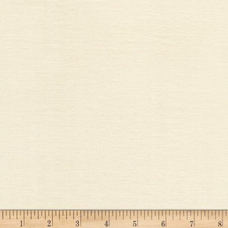 Pu&ograve; includere: Tessuto color crema con una sottile trama intrecciata. Il tessuto &egrave; di colore neutro e uniforme. Un righello di legno si trova nella parte inferiore dell'immagine, con misure in pollici.