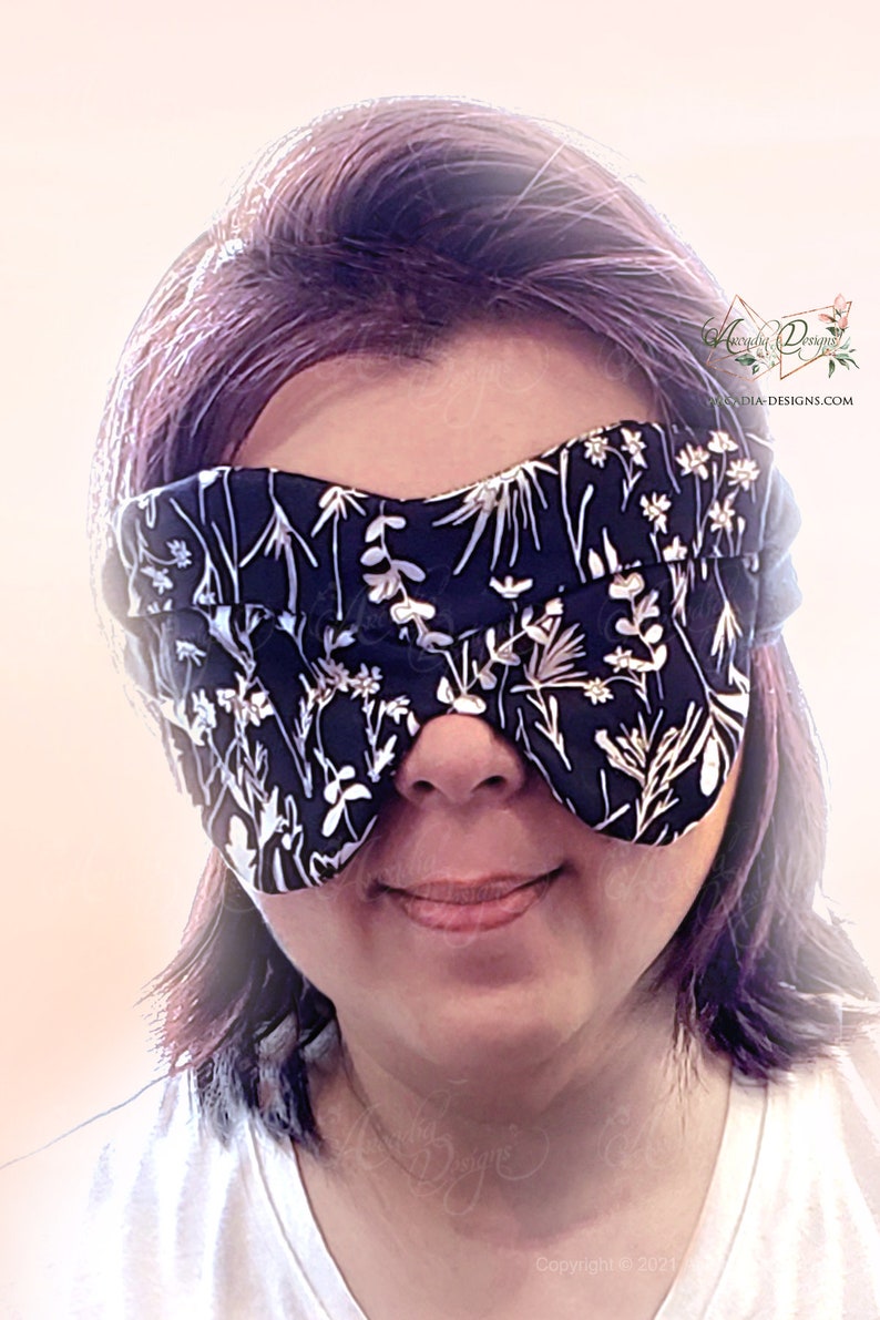 May include: A black sleep mask with a white floral pattern. The mask is worn by a person with short, purple hair.