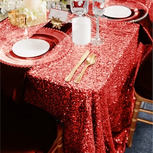 May include: Red sequin tablecloth with gold cutlery and white plates on a table set for a wedding reception.