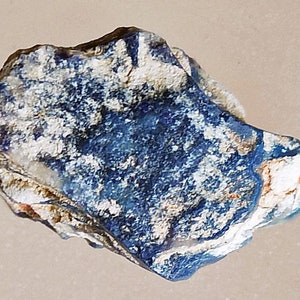 May include: A close-up of a blue and white stone with a rough, irregular shape. The stone has a mottled appearance with patches of white and blue.
