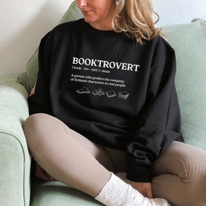 May include: Black sweatshirt with the text "BOOKTROVERT (book-tro-vert) - noun A person who prefers the company of fictional characters to real people." and a graphic of five open books.