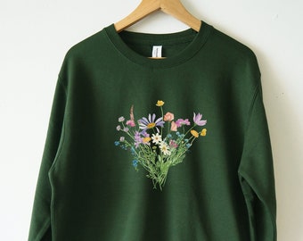 May include: A dark green sweatshirt with a floral print of a bouquet of wildflowers in shades of pink, purple, yellow, and blue.