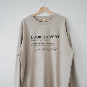 May include: A beige sweatshirt with the text "BOOKTROVERT (book-tro-vert) noun A person who prefers the company of fictional characters to real people." and a graphic of several open books.