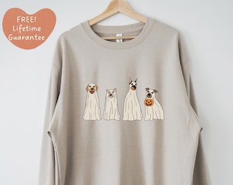 May include: A light beige sweatshirt featuring a graphic of four dogs dressed as ghosts for Halloween. The dogs are a golden retriever, a pig, a Doberman, and a terrier. The terrier is holding a pumpkin.