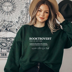 May include: A green sweatshirt with the text "BOOKTROVERT (book-tro-vert) noun A person who prefers the company of fictional characters to real people." and a graphic of four open books.