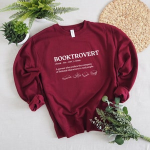 May include: Burgundy sweatshirt with a white graphic that reads "BOOKTROVERT (book-tro-vert) noun A person who prefers the company of fictional characters to real people."  The graphic also includes five small illustrations of open books.