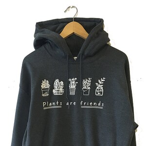 Könnte beinhalten: Ein dunkelgrauer Kapuzenpullover mit einer weißen Grafik von Topfpflanzen und dem Text "Plants are friends".