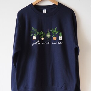 Puede incluir: Sudadera azul marino con un gr&aacute;fico blanco de plantas en maceta y el texto "just one more".