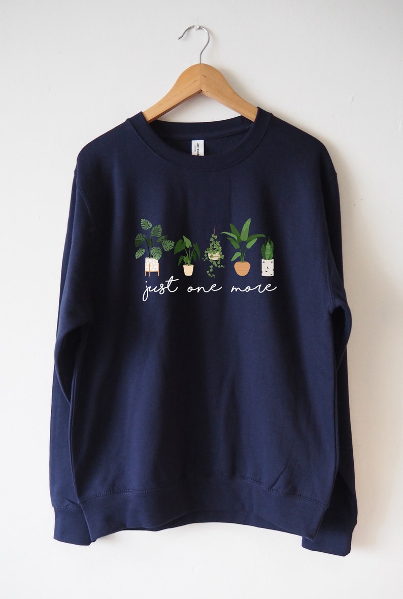 Puede incluir: Sudadera azul marino con un gr&aacute;fico blanco de plantas en maceta y el texto "just one more".