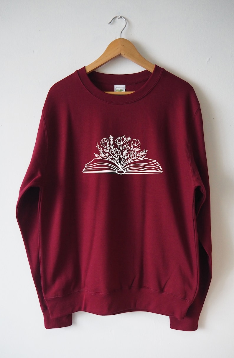 May include: A maroon sweatshirt with a white graphic of an open book with flowers growing out of it.