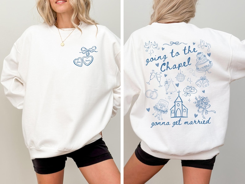 Może przedstawiać: Biała bluza z niebieskim wzorem w kształcie serca i imionami "Mom" i "Dad". Tył bluzy ma napis "going to the Chapel gonna get married" z ilustracjami o tematyce ślubnej.