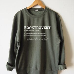 May include: A green sweatshirt with the word "BOOKTROVERT" printed on the front. The word is defined as "(book - tro - vert). noun A person who prefers the company of fictional characters to real people."