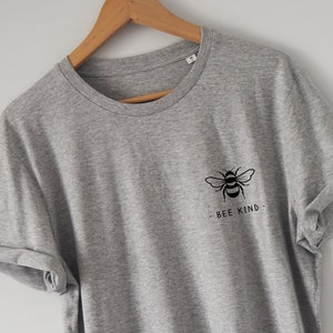 Może przedstawiać: Szary t-shirt z czarnym nadrukiem pszczoły i tekstem "BEE KIND" z przodu.