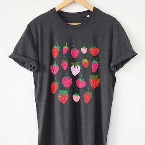 Puede incluir: Una camiseta gris oscuro con un patr&oacute;n de fresas rojas, rosas y verdes. Las fresas est&aacute;n dispuestas en un patr&oacute;n de cuadr&iacute;cula en la parte delantera de la camiseta.