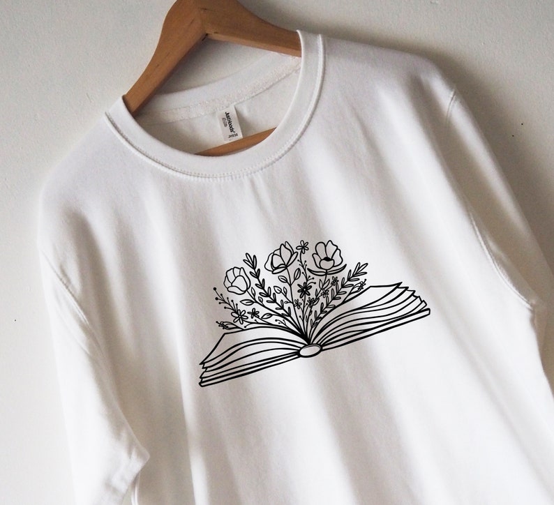 May include: White sweatshirt with a black line drawing of an open book with flowers growing out of it.