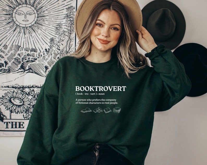 May include: A green sweatshirt with the text "BOOKTROVERT (book-tro-vert) noun A person who prefers the company of fictional characters to real people." and a graphic of four open books.
