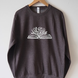 May include: A dark gray sweatshirt with a white graphic of an open book with flowers growing out of it.