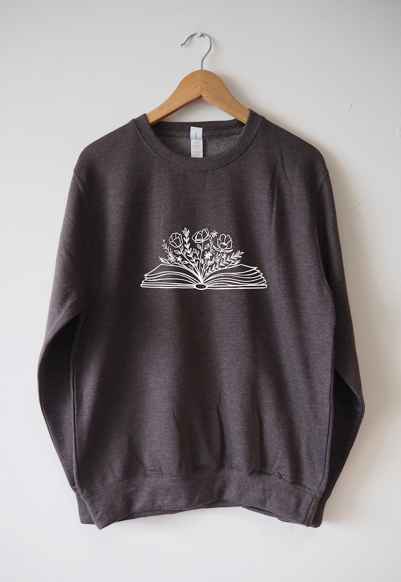 May include: A dark gray sweatshirt with a white graphic of an open book with flowers growing out of it.