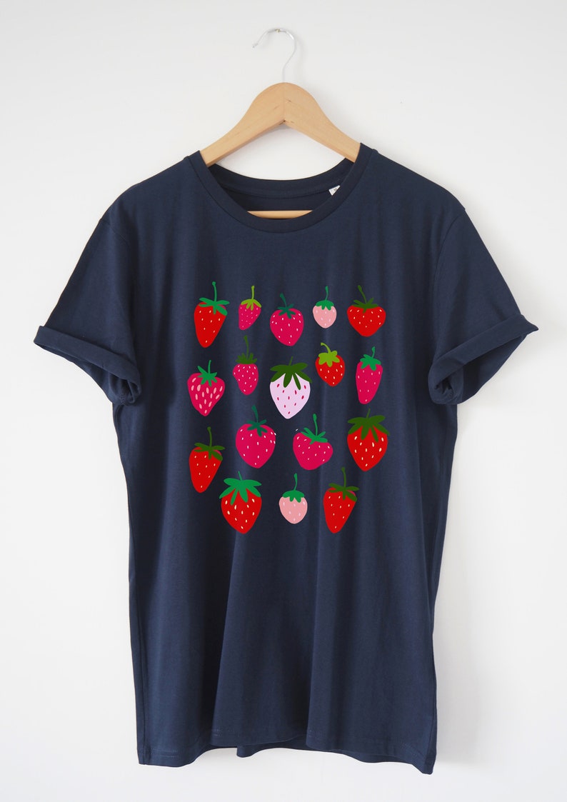 Puede incluir: Una camiseta azul marino con un patr&oacute;n de fresas rojas, rosas y verdes.