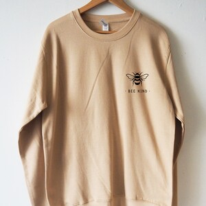May include: A beige sweatshirt with a black bee graphic and the text "Bee Kind" on the front.