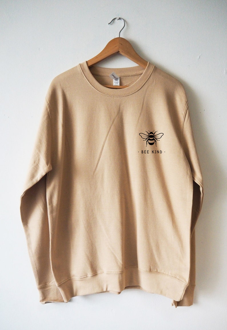 May include: A beige sweatshirt with a black bee graphic and the text "Bee Kind" on the front.