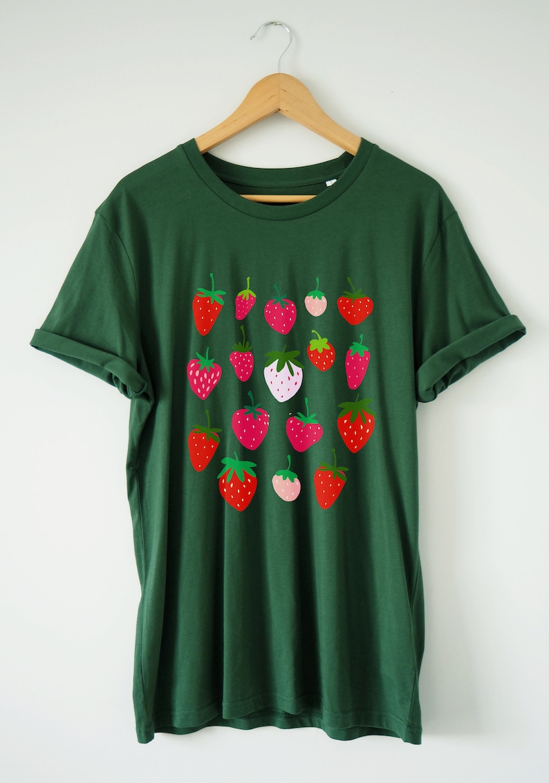Puede incluir: Una camiseta verde oscuro con un estampado gr&aacute;fico de fresas rojas, rosas y blancas. Las fresas est&aacute;n dispuestas en una cuadr&iacute;cula en la parte delantera de la camiseta.