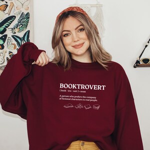 May include: A maroon sweatshirt with the word "BOOKTROVERT" printed on the front. The word is defined as "(book-tro-vert) noun A person who prefers the company of fictional characters to real people."