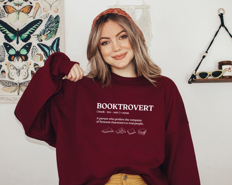 May include: A maroon sweatshirt with the word "BOOKTROVERT" printed on the front. The word is defined as "(book-tro-vert) noun A person who prefers the company of fictional characters to real people."