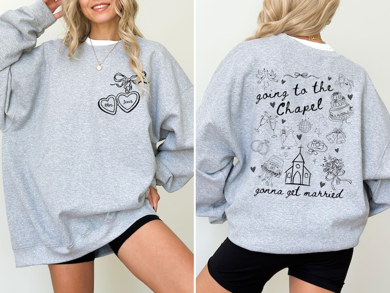 Może przedstawiać: Jasnoszara bluza z napisem "going to the Chapel gonna get married" i ilustracjami o tematyce ślubnej z tyłu. Z przodu dwa wisiorki w kształcie serca z napisami "Mrs" i "June".