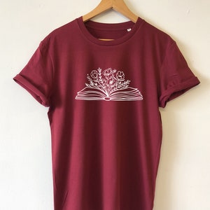 May include: A maroon t-shirt with a white graphic of an open book with flowers growing out of it.