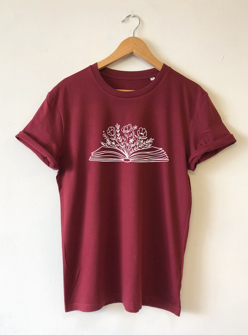 May include: A maroon t-shirt with a white graphic of an open book with flowers growing out of it.