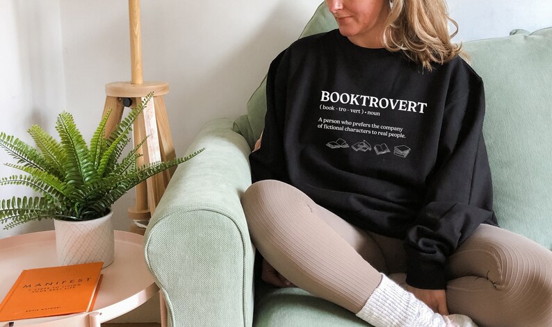 May include: Black sweatshirt with the text "BOOKTROVERT (book-tro-vert) - noun A person who prefers the company of fictional characters to real people." and a graphic of five open books.