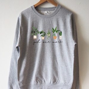 Puede incluir: Sudadera gris con un gr&aacute;fico de plantas en maceta y el texto "just one more".