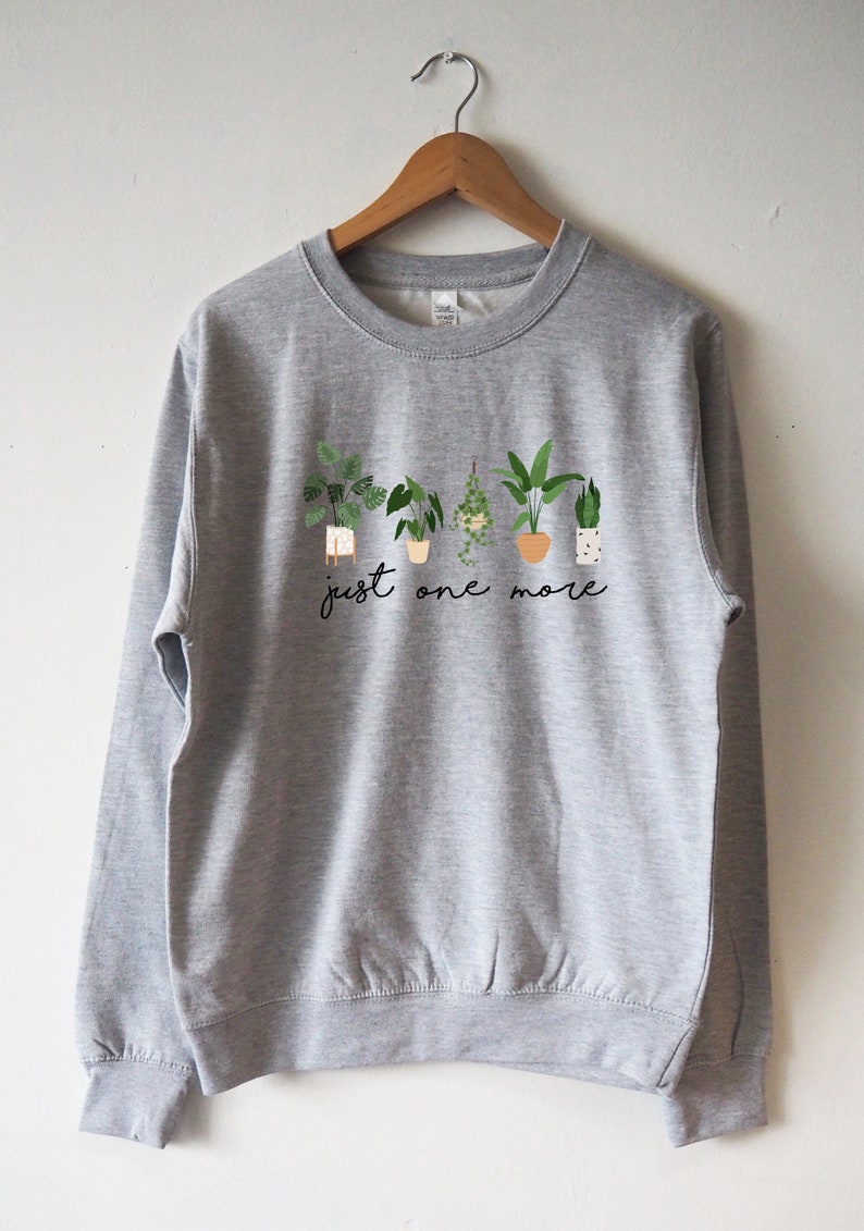 Puede incluir: Sudadera gris con un gr&aacute;fico de plantas en maceta y el texto "just one more".