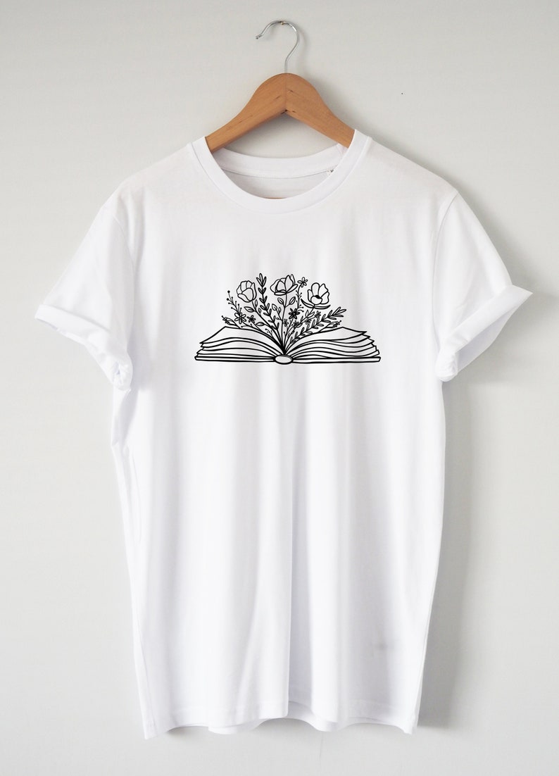 May include: White t-shirt with a black line drawing of an open book with flowers growing out of it.
