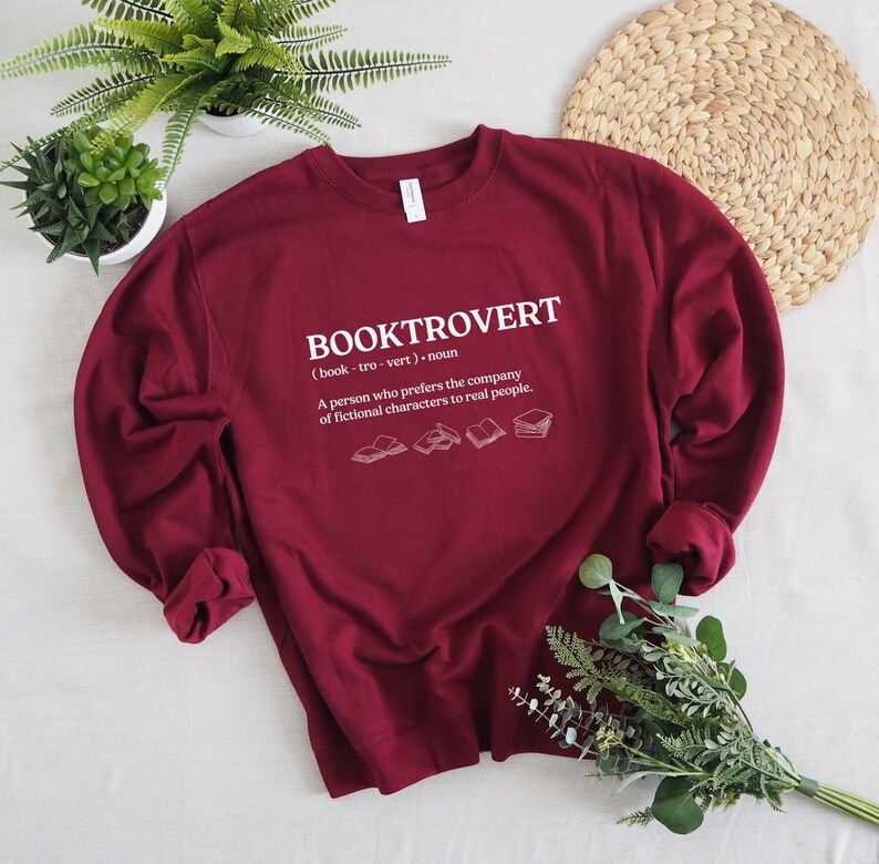 May include: Burgundy sweatshirt with a white graphic that reads "BOOKTROVERT (book-tro-vert) noun A person who prefers the company of fictional characters to real people."  The graphic also includes five small illustrations of open books.