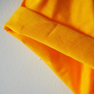 May include: Close-up of a bright yellow fabric with a folded edge. The fabric has a textured, ribbed surface.