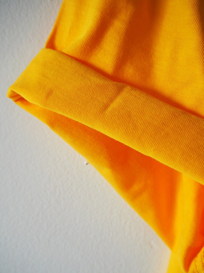 May include: Close-up of a bright yellow fabric with a folded edge. The fabric has a textured, ribbed surface.