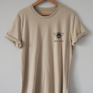 May include: A beige t-shirt with a black bee graphic and the text "BEE KIND" on the front.